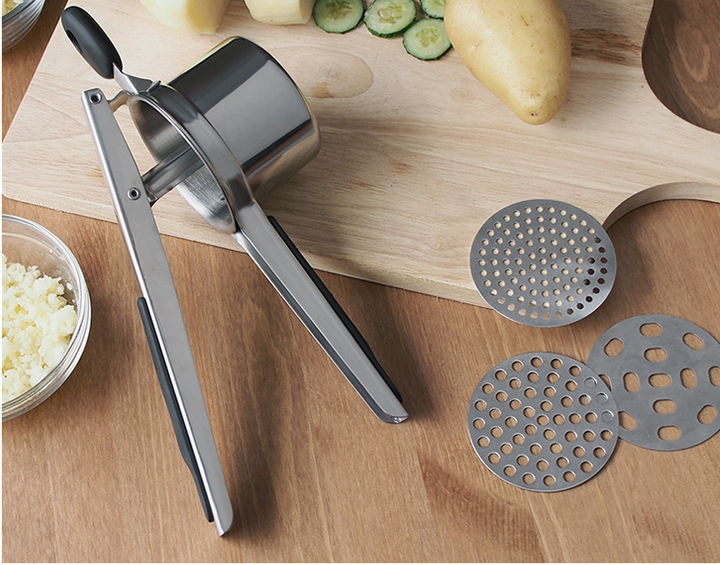 Potato ricer on a cutting board with potatoes and discs