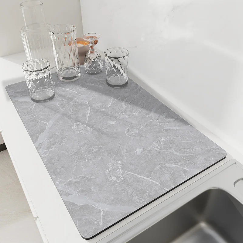 Light gray marble stone dish drying mat on a kitchen counter beside a sink